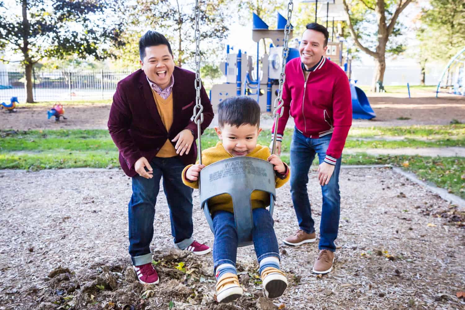 Two fathers pushing little boy on swing set