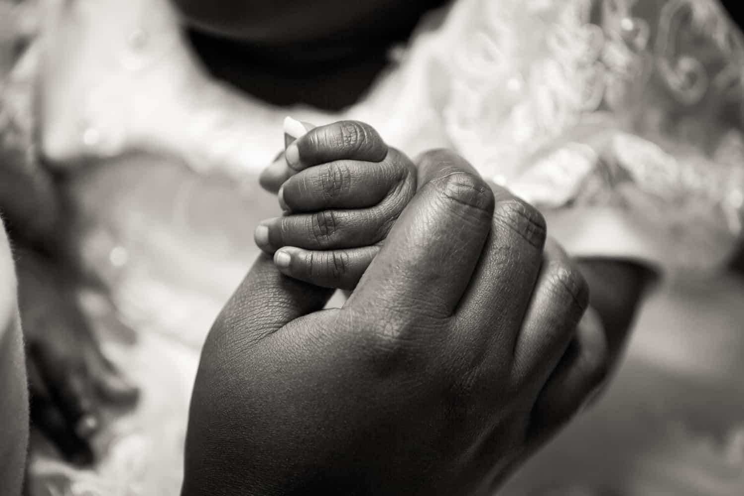 Black and white photo of mother's hand holding baby hand