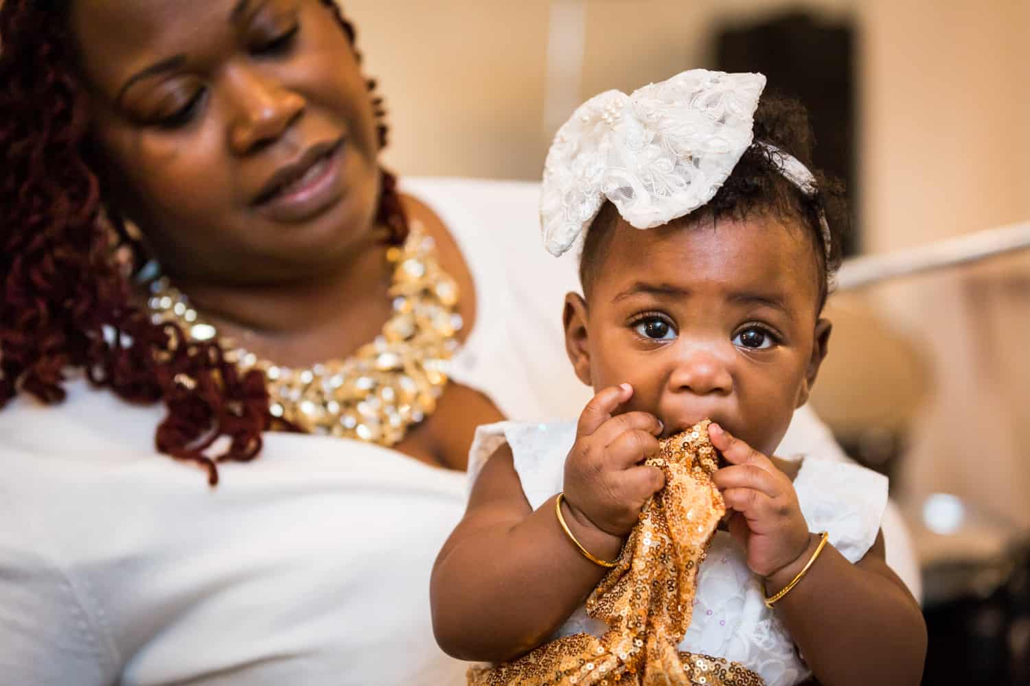African American baby girl chewing on gold sequin sash