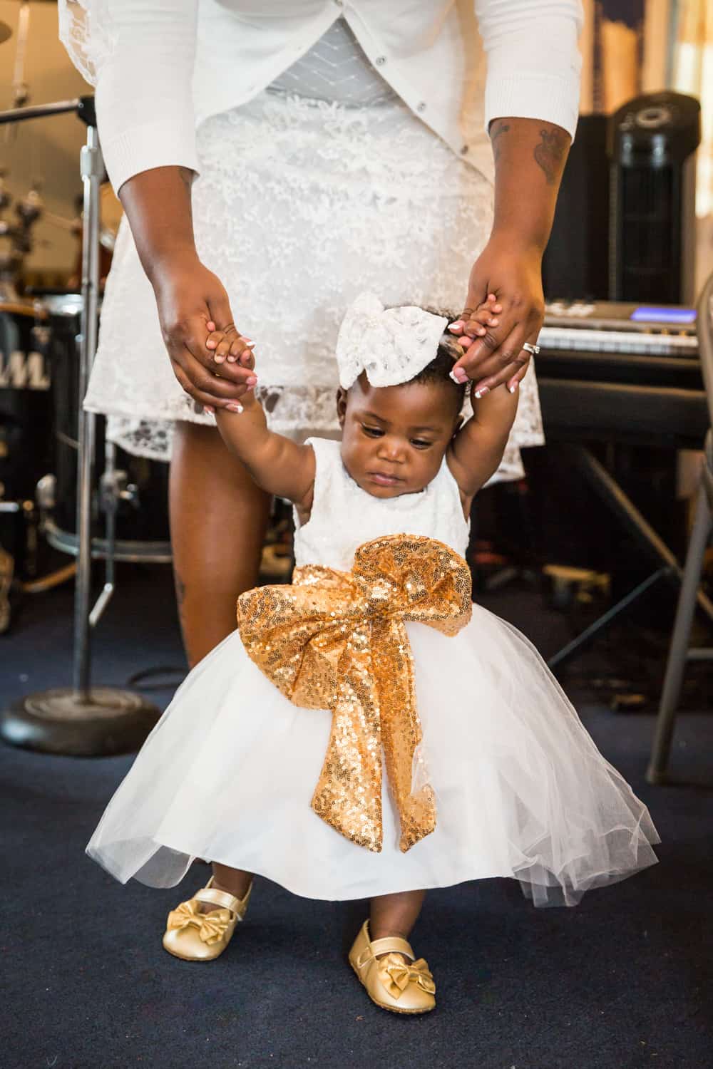 Mother's hands holding baby girl wearing white dress and gold sash