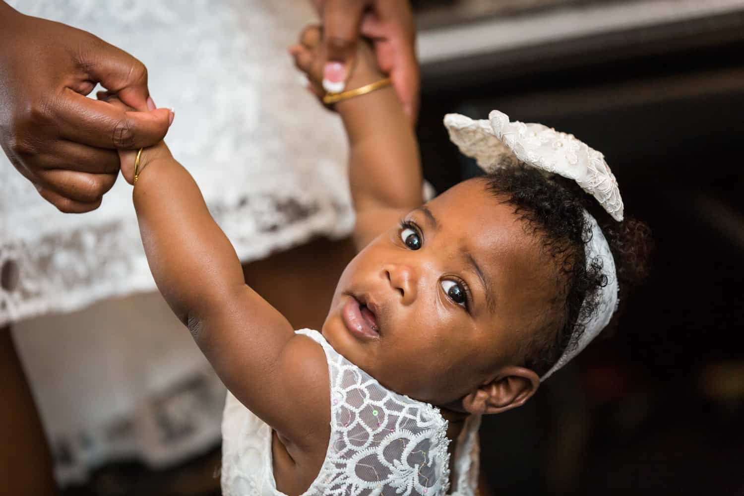 Hands holding African American baby girl wearing white dress and bow