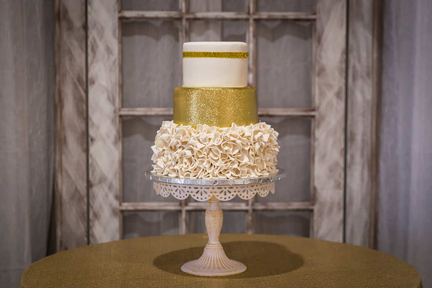 Wedding cake on cake stand with intricate icing and gold glitter