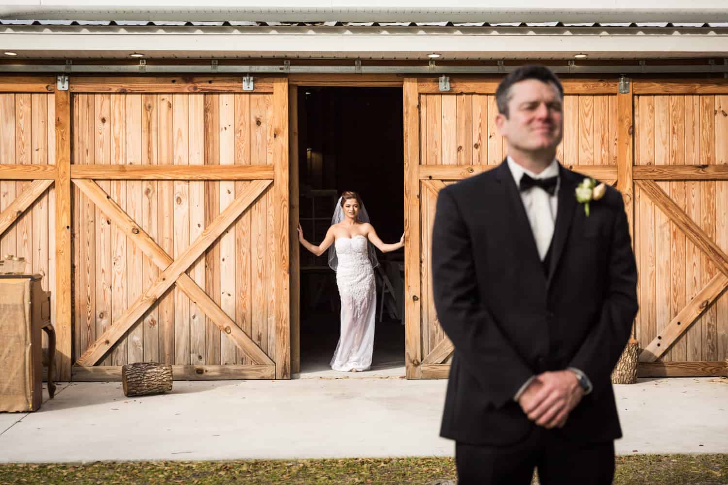 Bride looking through barn door at groom with back turned
