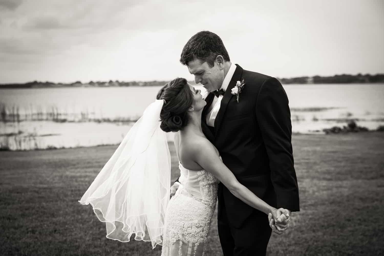 Black and white photo of bride and groom holding hands in front of lake for an article on wedding cost cutting tips