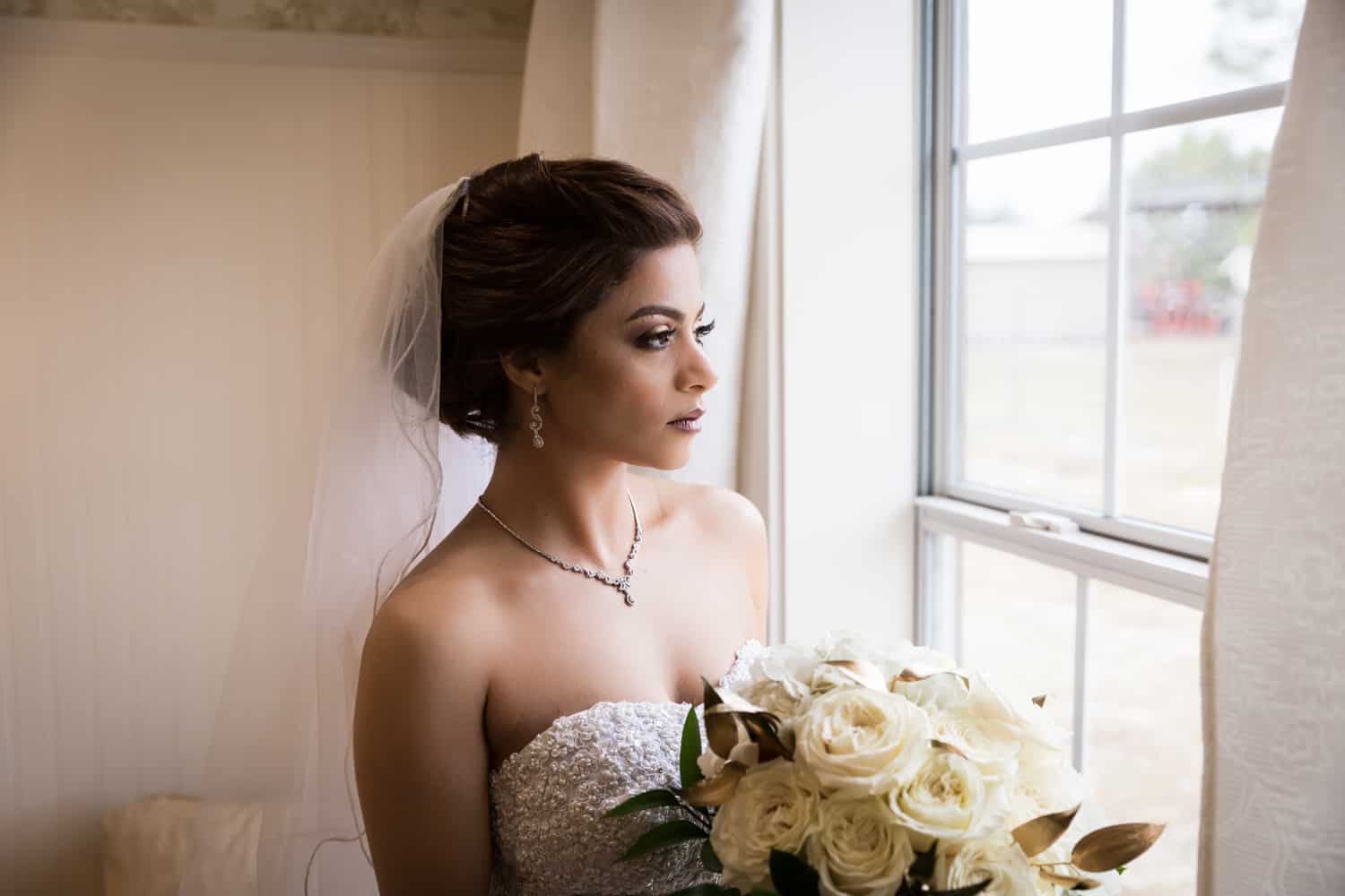Bride holding bouquet and looking out window for an article on wedding cost cutting tips