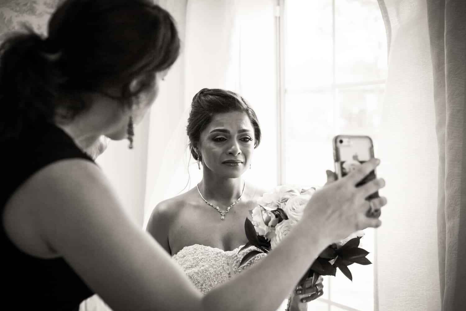 Black and white photo of bride crying and watching cell phone