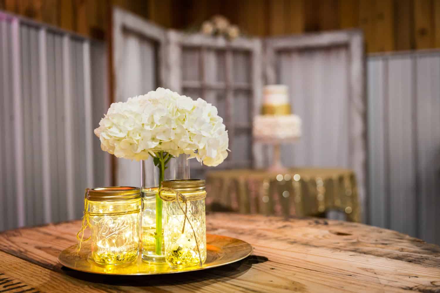 Tray of mason jars filled with fairy lights and vase of white hydrangeas