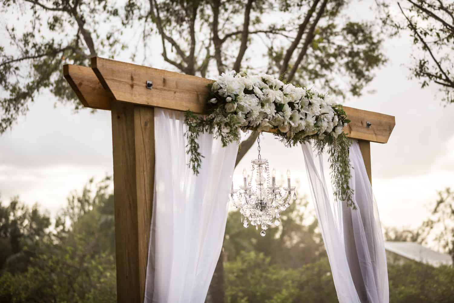 Wooden archway with white curtains, flowers, and a chandelier
