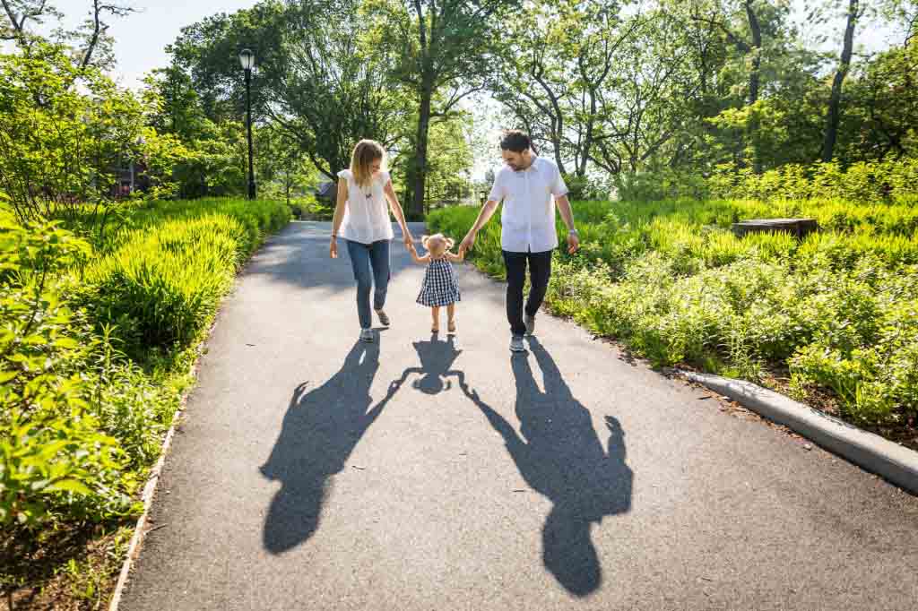 Parents walking with little girl casting huge shadow on sidewalk