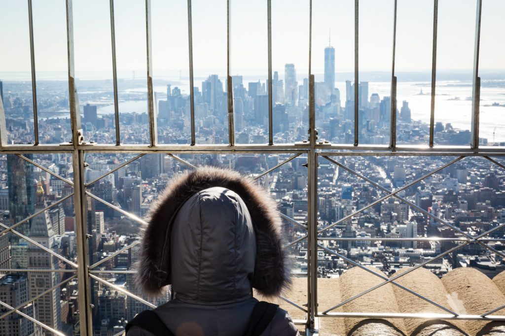 Person wearing fur hood looking at view of NYC from top of Empire State Buillding