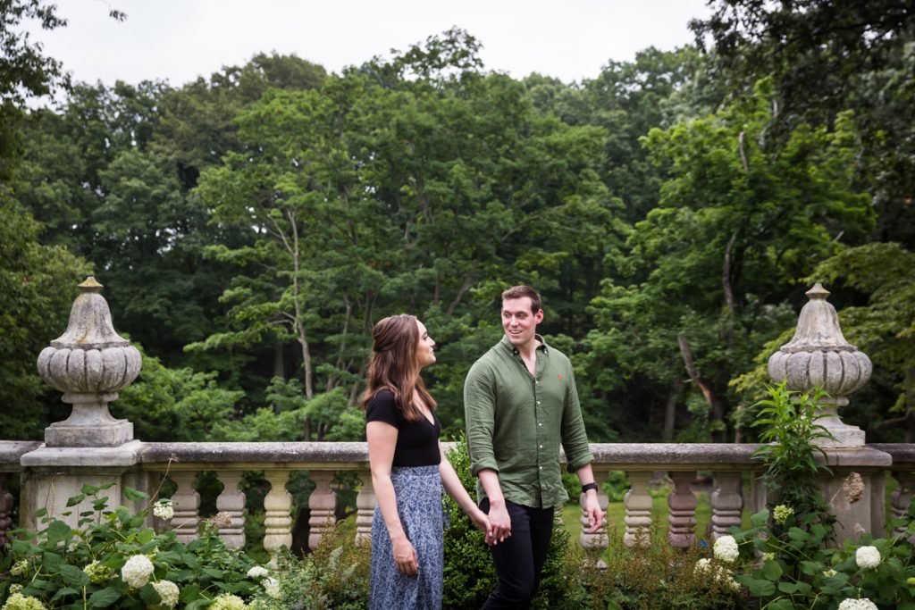 Vanderbilt Museum engagement photos of couple walking in front of stone railing and forest