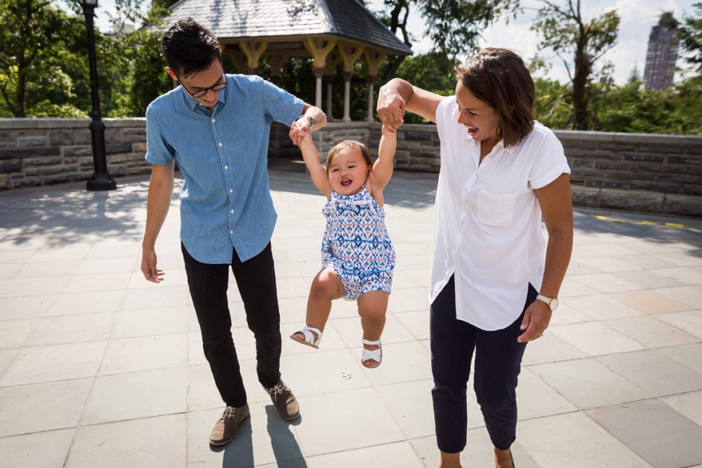 Mother and father swinging toddler by arms during Belvedere Castle family portrait in Central Park