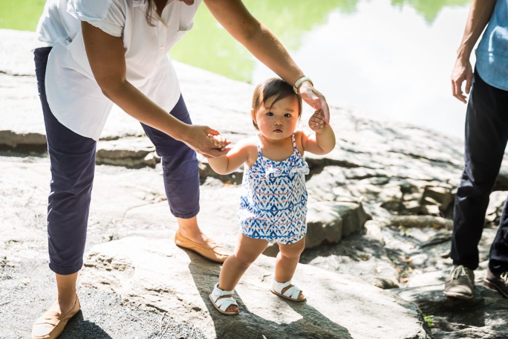 Mother helping baby girl walk on rock in Central Park