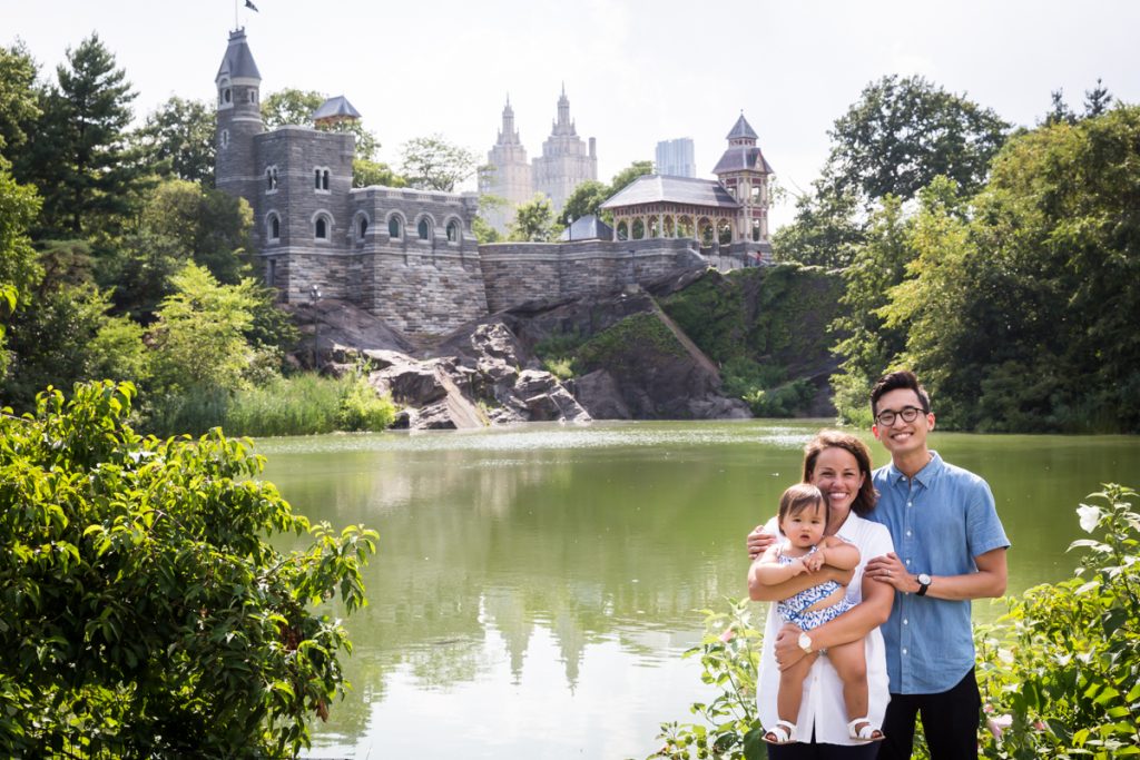 Mother and father holding baby in front of Turtle Pond and Belvedere Castle