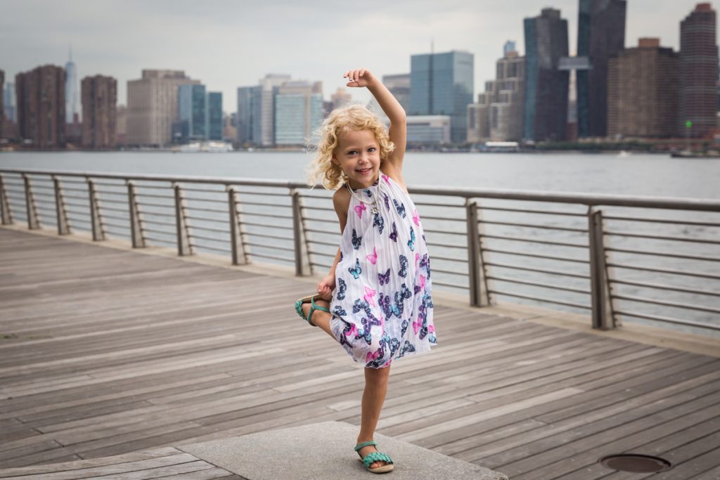Little girl with blond hair holding foot during a Gantry Plaza family portrait session