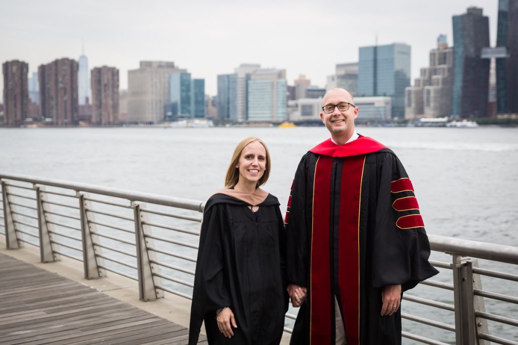 Couple dressed in graduation robes on boardwalk during a Gantry Plaza family portrait session