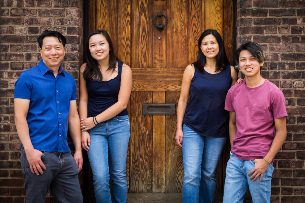 Family standing in front of brick wall and wooden door for an article on photo tips for older children