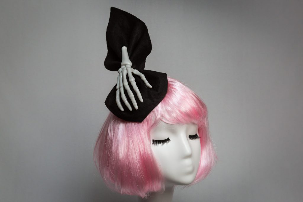 Pink haired mannequin wearing black felt and skeleton hand fascinator
