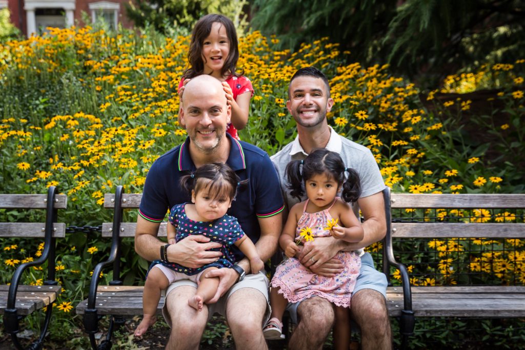 Two fathers and their three daughters sitting on bench during a Washington Square Park family portrait