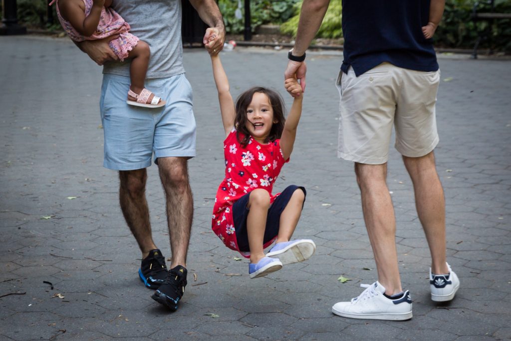 Little girl being swung by arms of two fathers