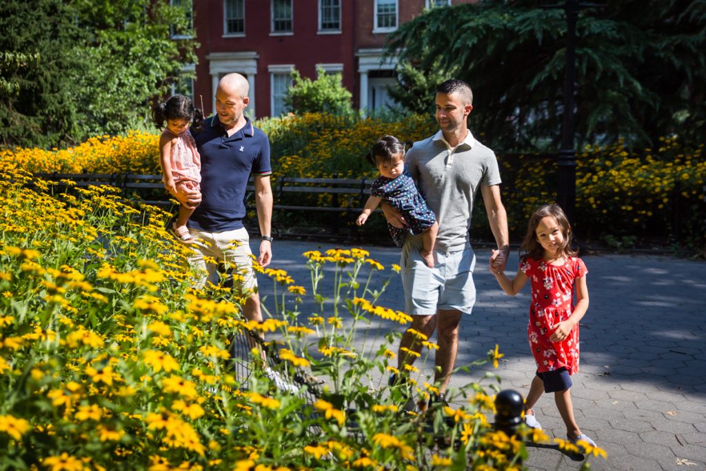 Two fathers and their daughters walking in front of yellow daisies during Washington Square Park family portrait