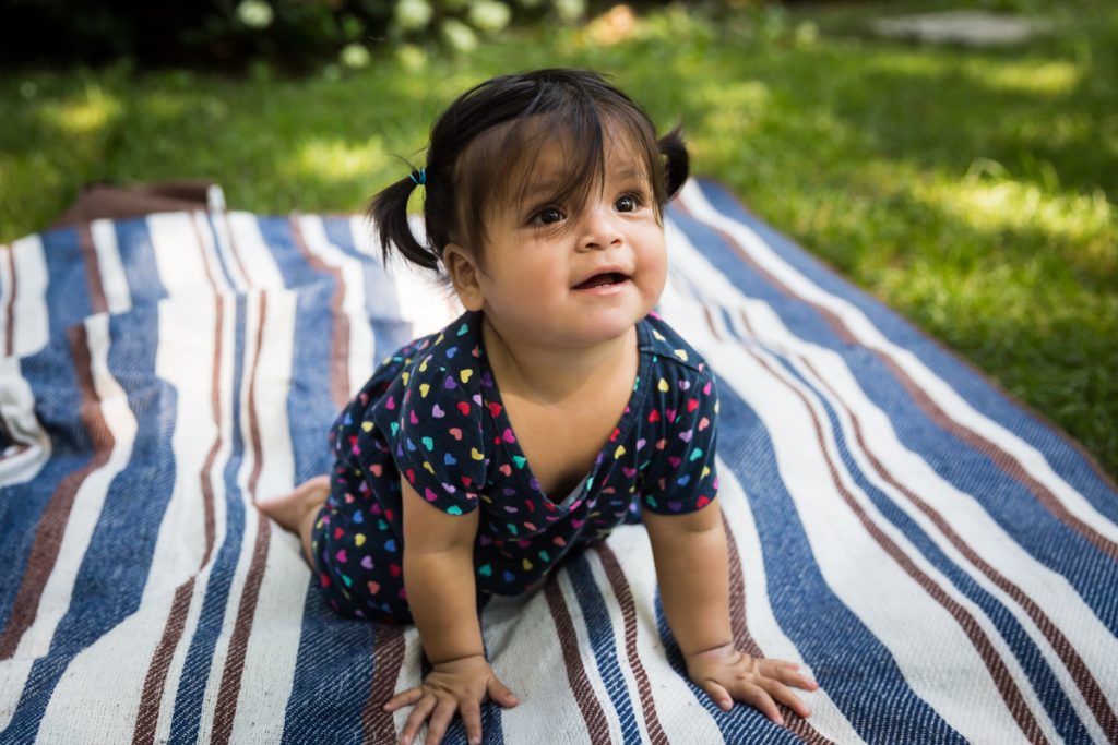 Toddler with pigtails crawling on striped blanket