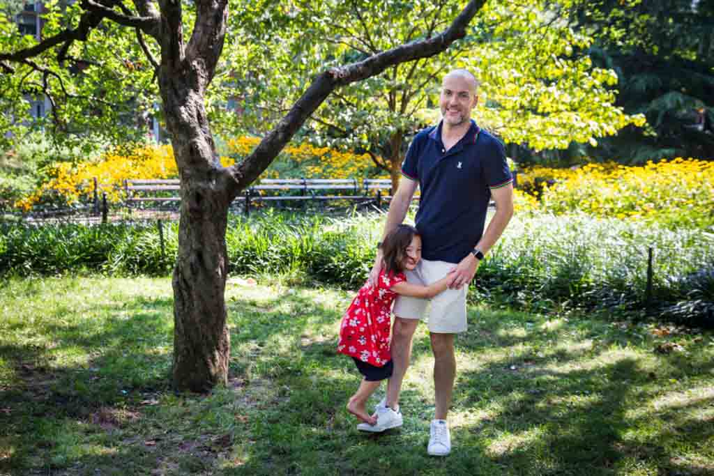 Father walking with daughter on his leg during a Washington Square Park family portrait