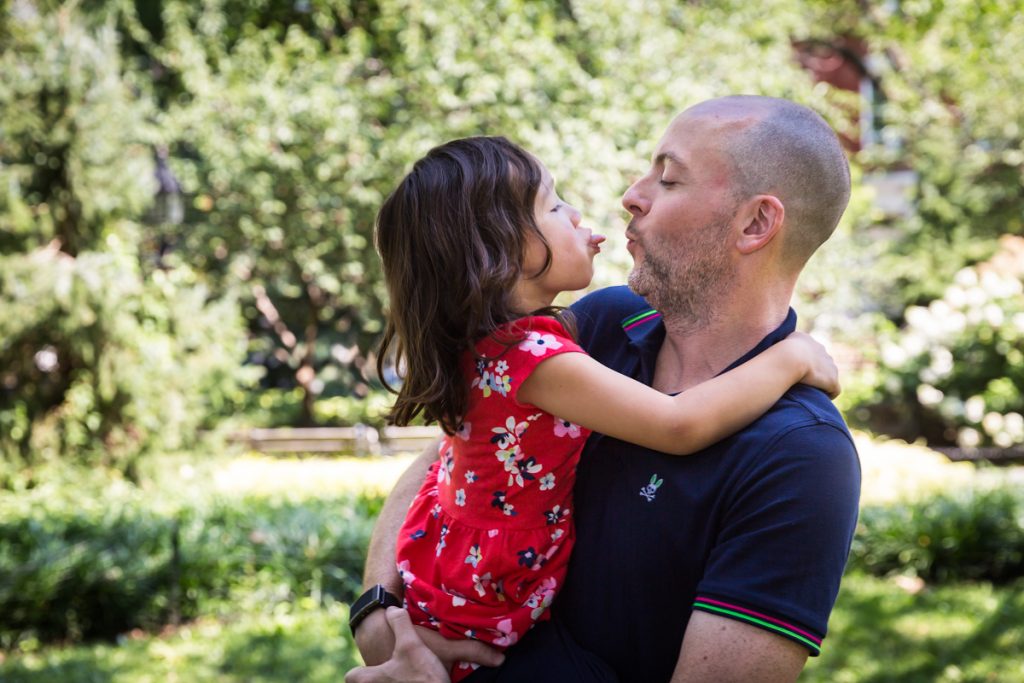 Father about to kiss daughter during a Washington Square Park family portrait