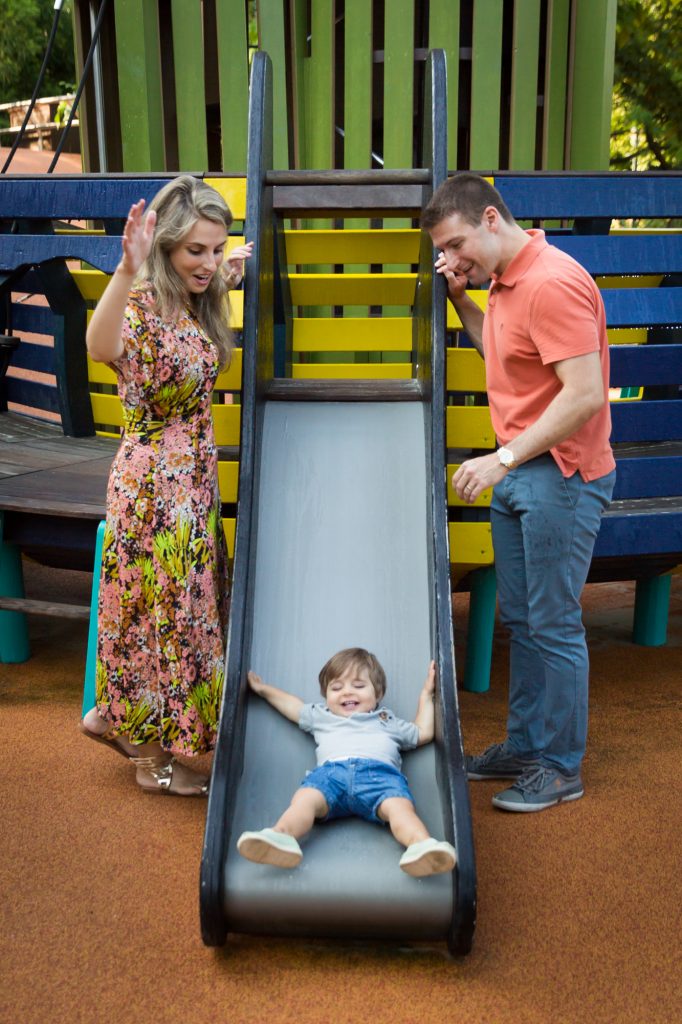 Parents watching little boy go down slide during a Chelsea Waterside Park family portrait session