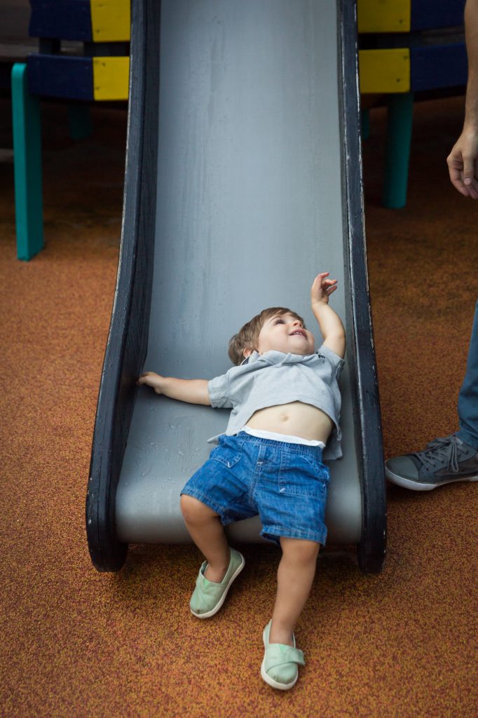 Little boy laying on slide during a Chelsea Waterside Park family portrait session