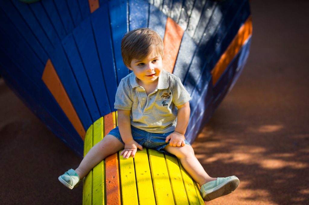 Little boy sitting on blue and yellow wooden snake during a Chelsea Waterside Park family portrait session