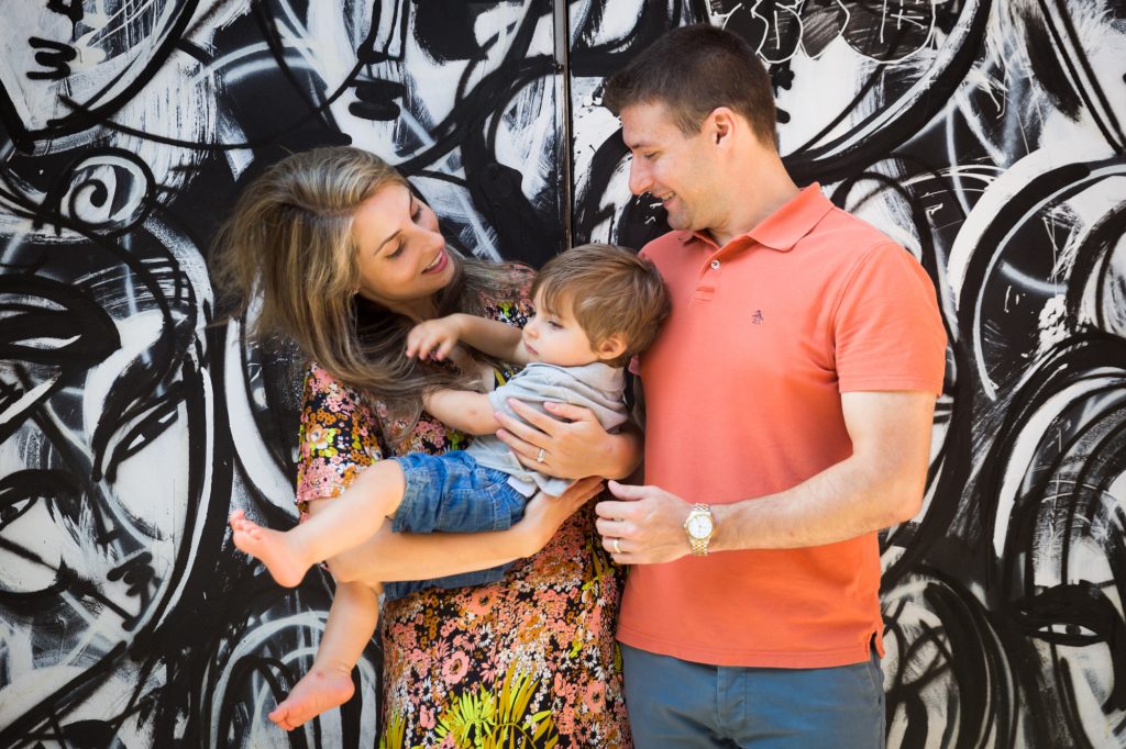 Parents holding little boy in front of black and white graffiti wall