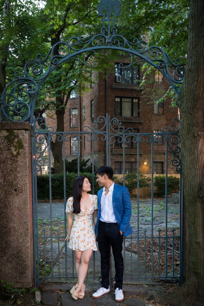 Couple standing in front of creepy iron gate during Queens engagement photo session