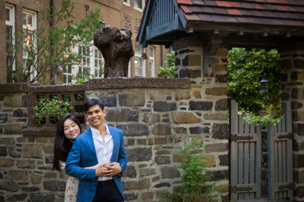 Couple hugging in front of stone wall and small gate during Forest Hills engagement shoot
