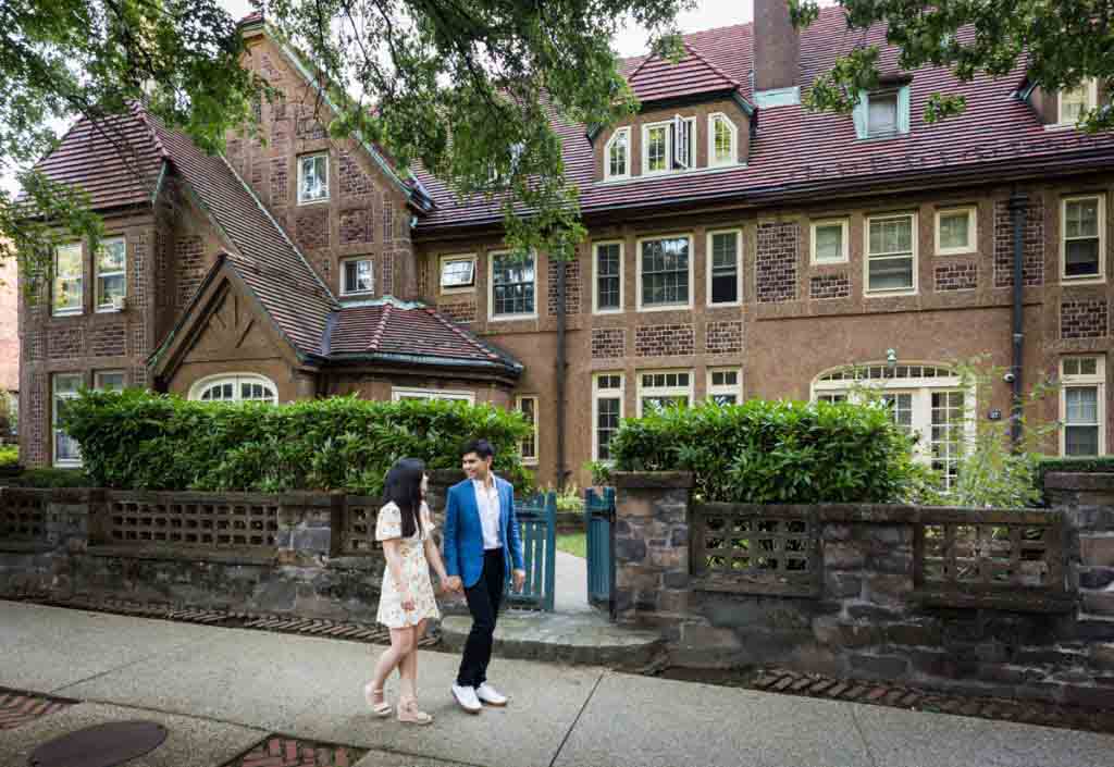 Couple walking past Tudor-style home during Forest Hills engagement shoot