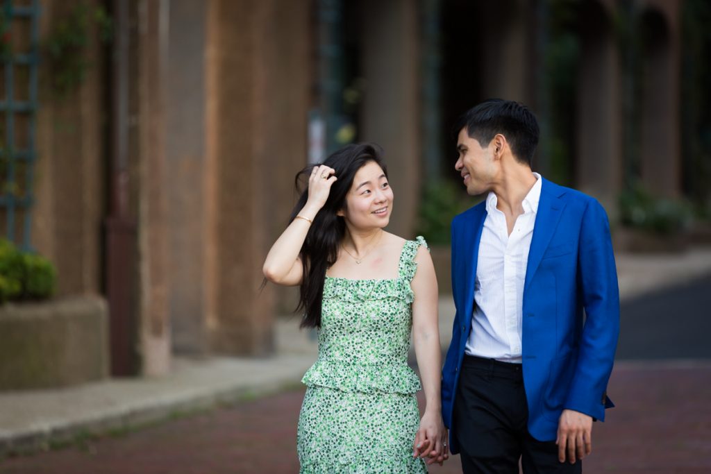 Woman touching hair while walking with man during Forest Hills engagement session