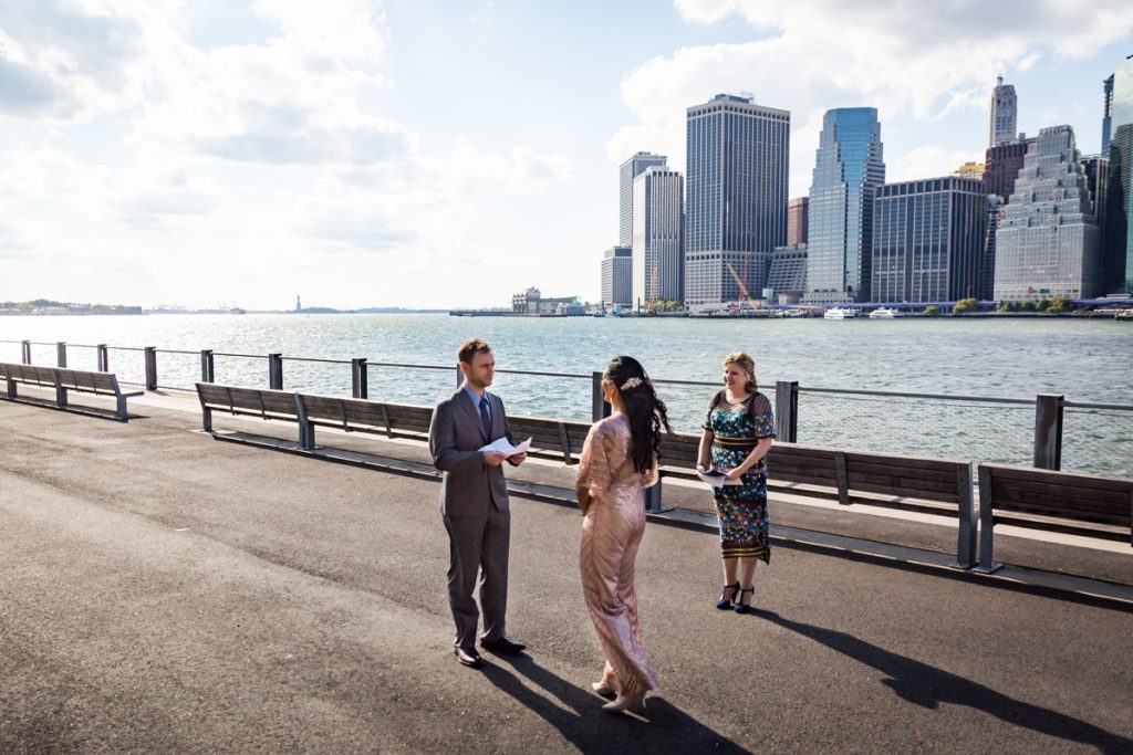 Bride and groom saying vows in front of NYC skyline for an article on how to get married in Brooklyn Bridge Park