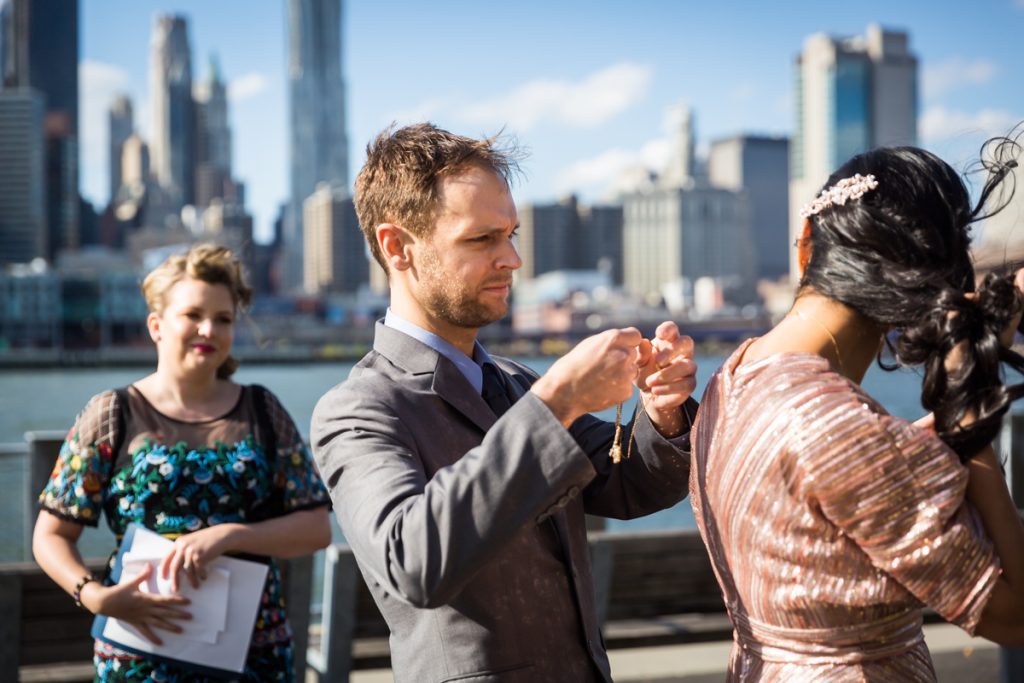 Groom putting necklace on Indian bride during Brooklyn Bridge Park wedding