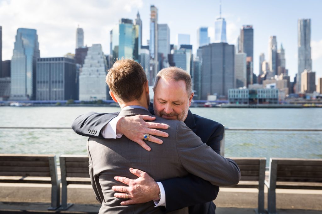 Father hugging groom during Brooklyn Bridge Park wedding ceremony