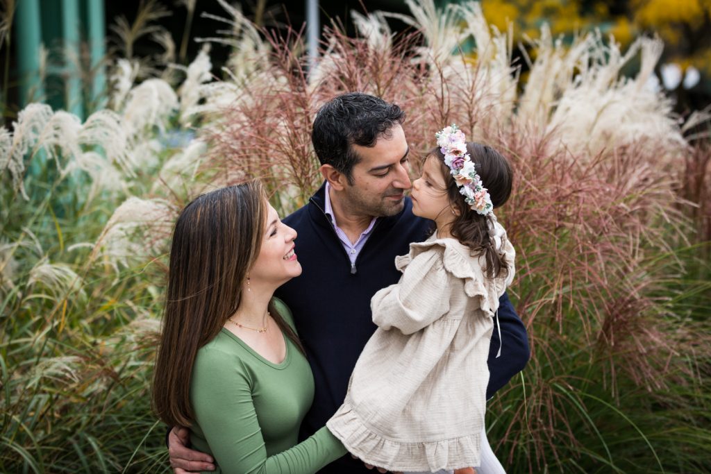 Mother watching little girl and father give 'nose kisses' in front of pink bush