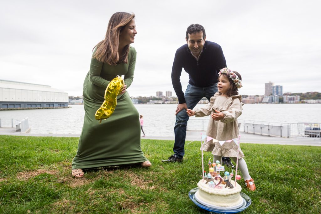Parents playing with little girl in front of birthday cake