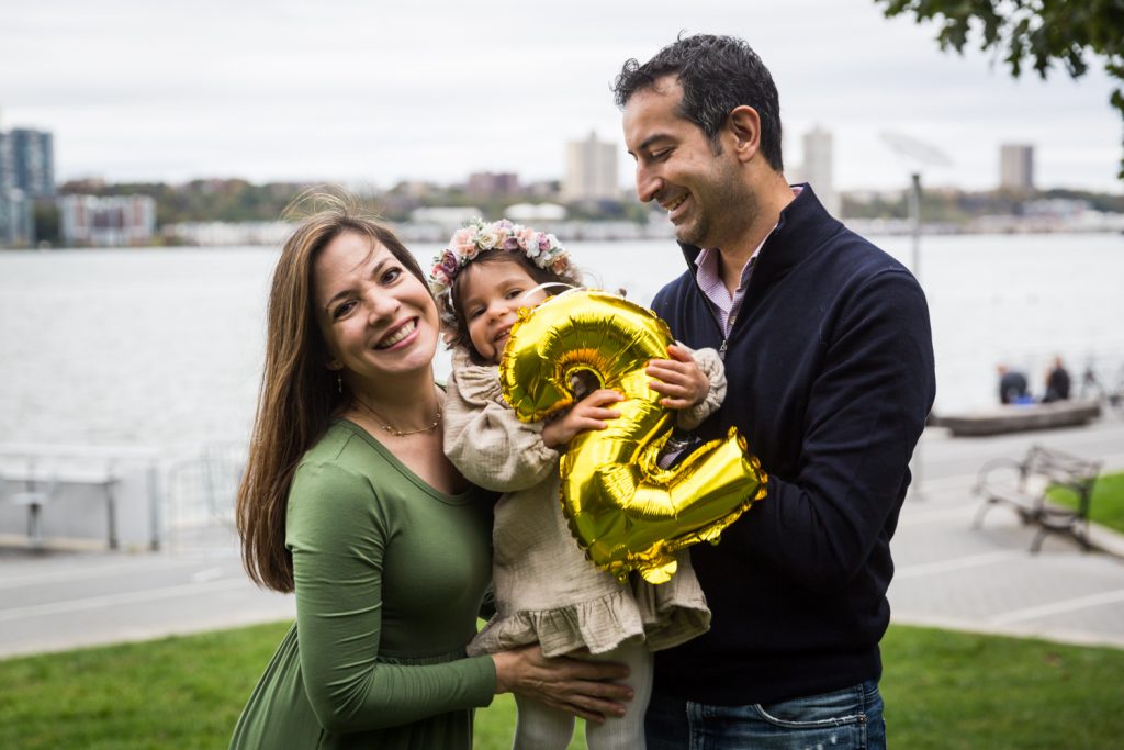 Parents holding little girl holding gold number 2 balloon