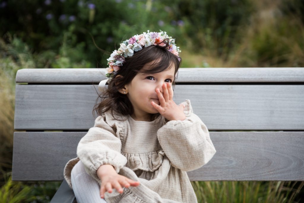 LIttle girl with hand to face wearing flower crown in Waterline Square Park