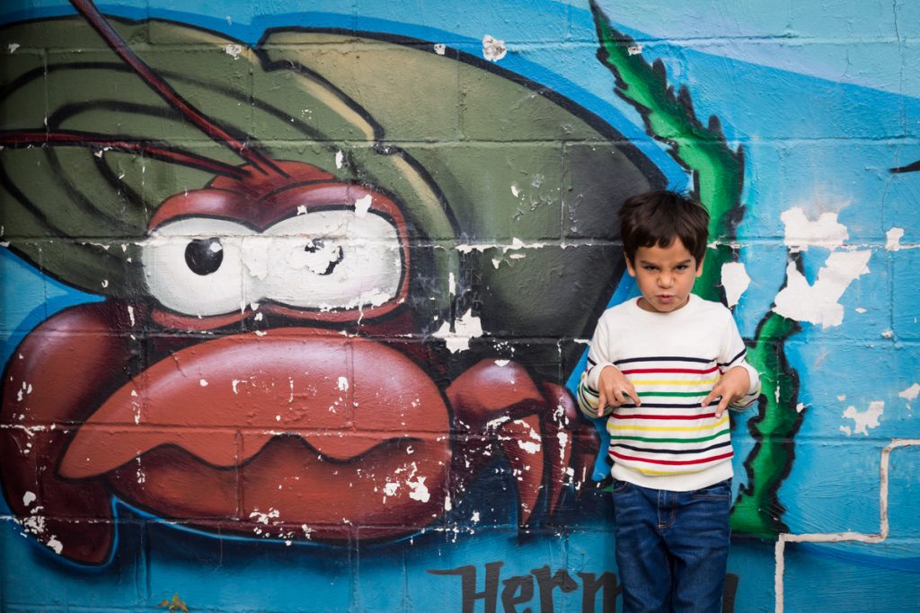 Little boy making crab face in front of colorful sea life mural
