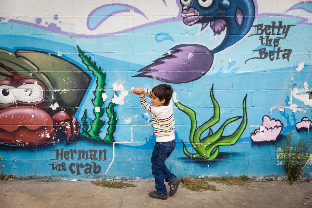 Little boy playing shark in front of ocean life mural