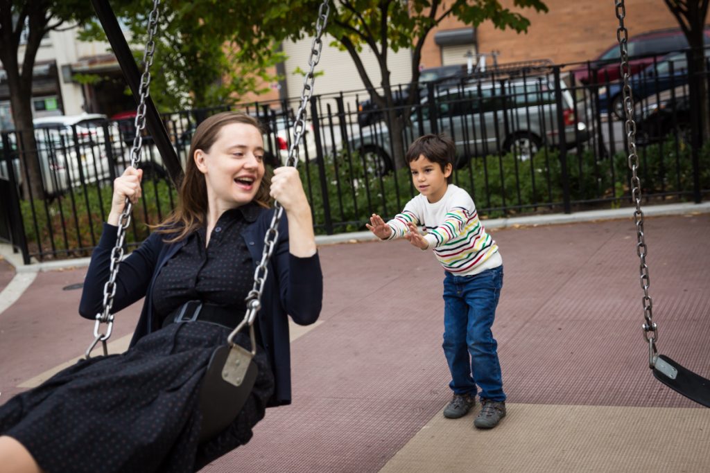 Boy pushing mother in swing during a Gowanus family portrait session