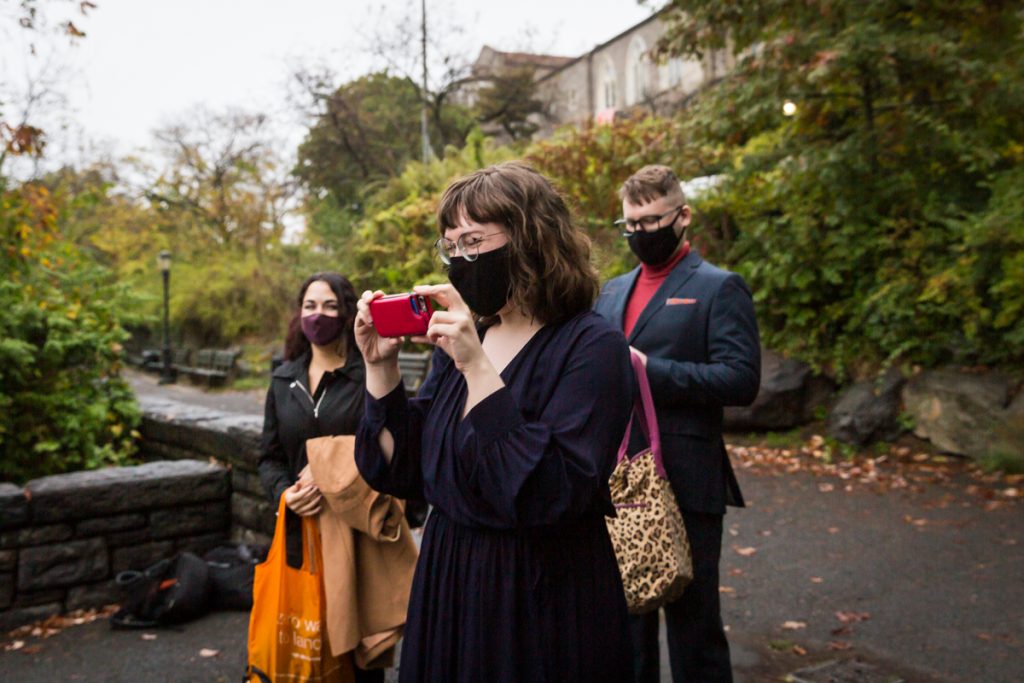 Wedding guests wearing masks and taking photos with cell phone at Fort Tryon Park wedding