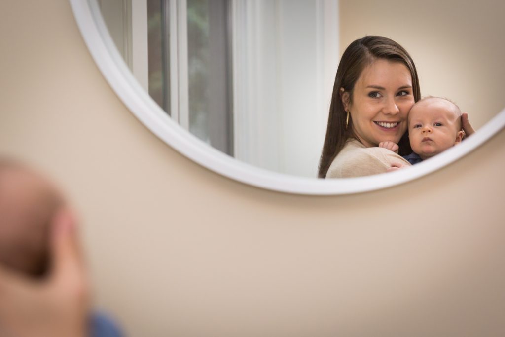 Mother and newborn baby looking into mirror for an article on how to prepare for a newborn portrait session