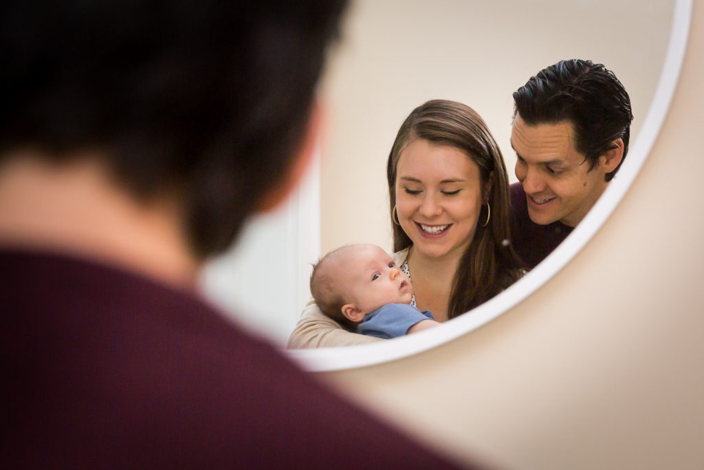 Reflection in mirror of parents looking at newborn baby for an article on how to prepare for a newborn portrait session