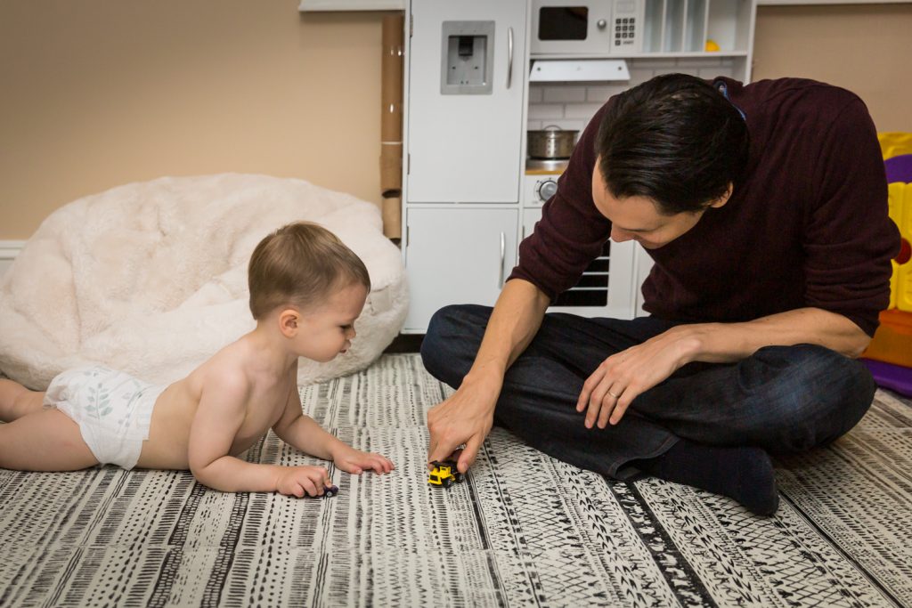 Father playing toy cars with little boy on carpet